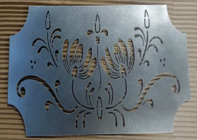 Decorative metal plate with cut-out floral design on a wooden surface.